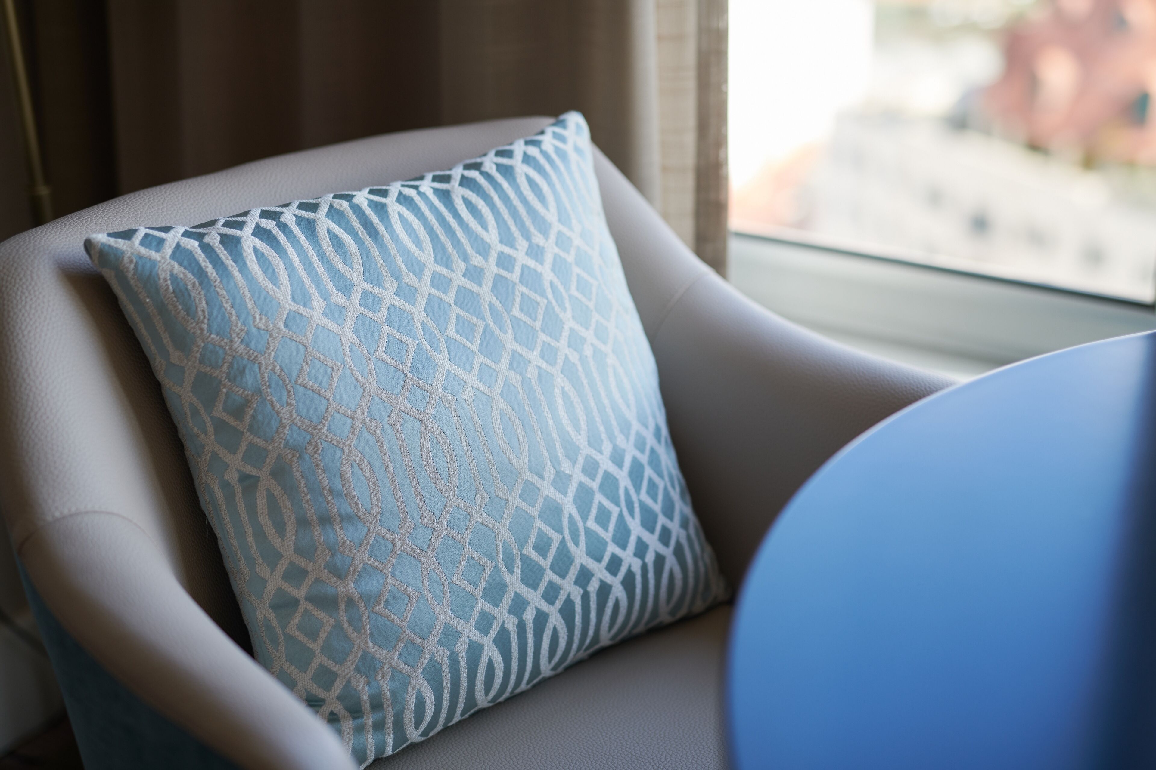 A chair with a patterned cushion and a window with a view of buildings.