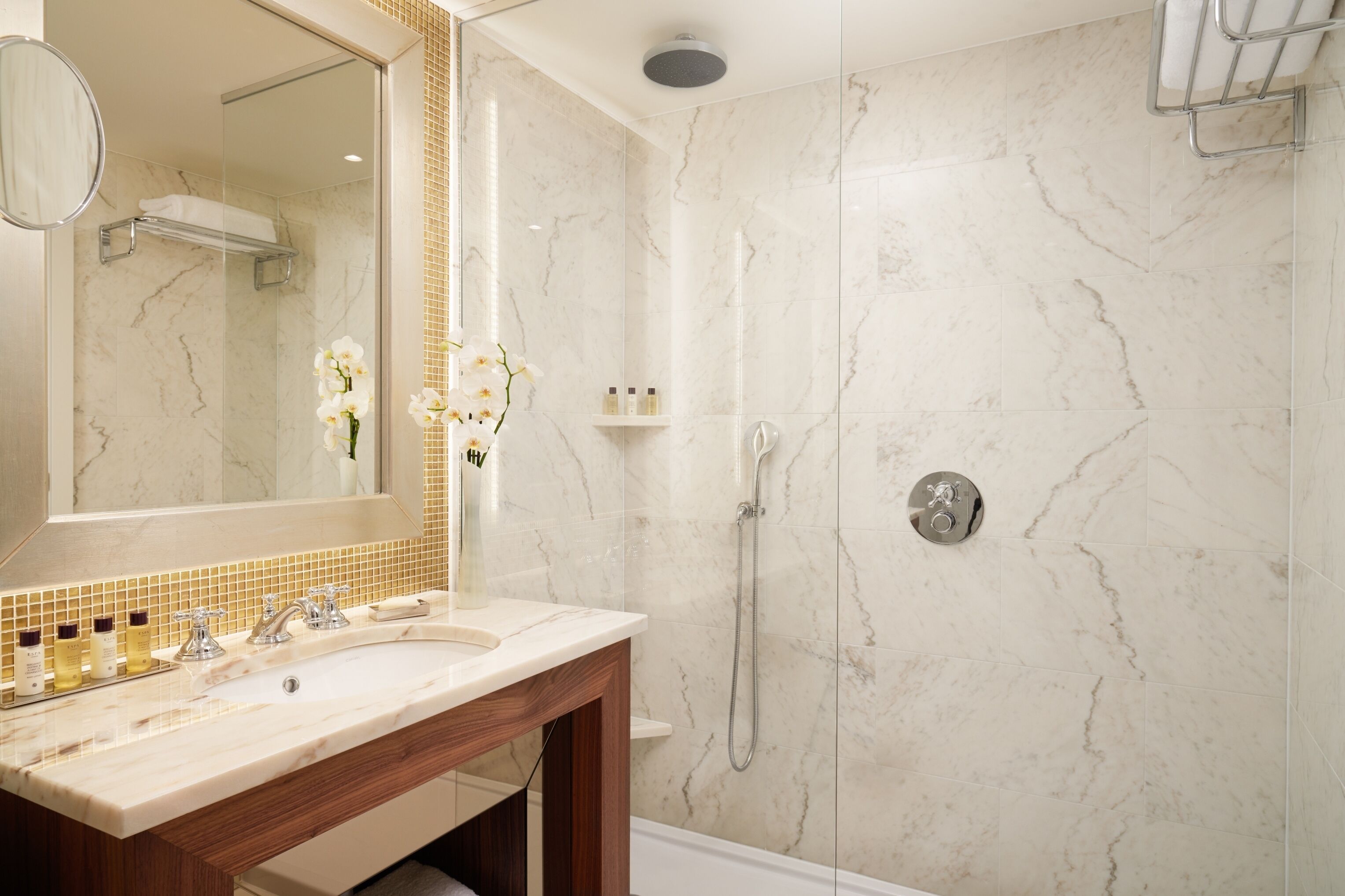 Un baño moderno con un lavabo de mármol, ducha con cerramiento de vidrio y un espejo grande.