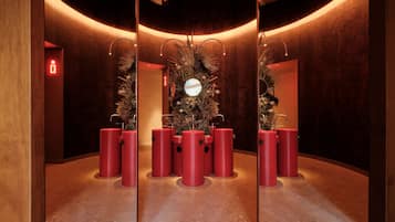 Un baño moderno con un espejo central, taburetes cilíndricos rojos y un arreglo floral.