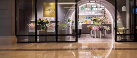 Fachada con entrada de vidrio, mostrando arreglos florales y diversos artículos en estanterías.