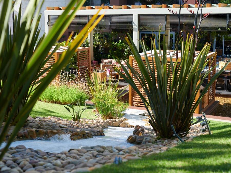 A garden pathway with rocks and plants, outdoor seating, and a building with a covered patio area.