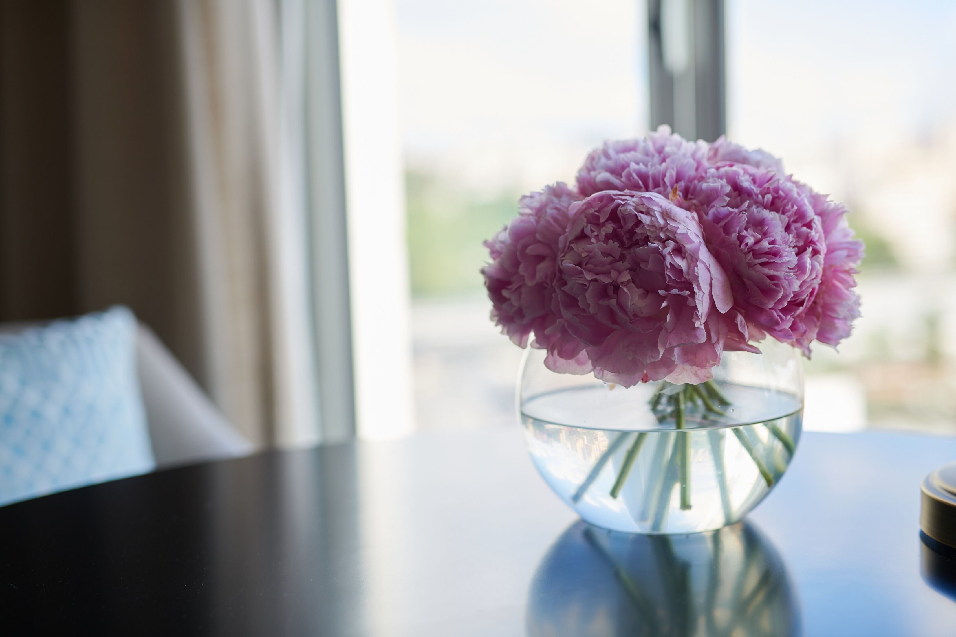 A vase with pink flowers on a table near a window.