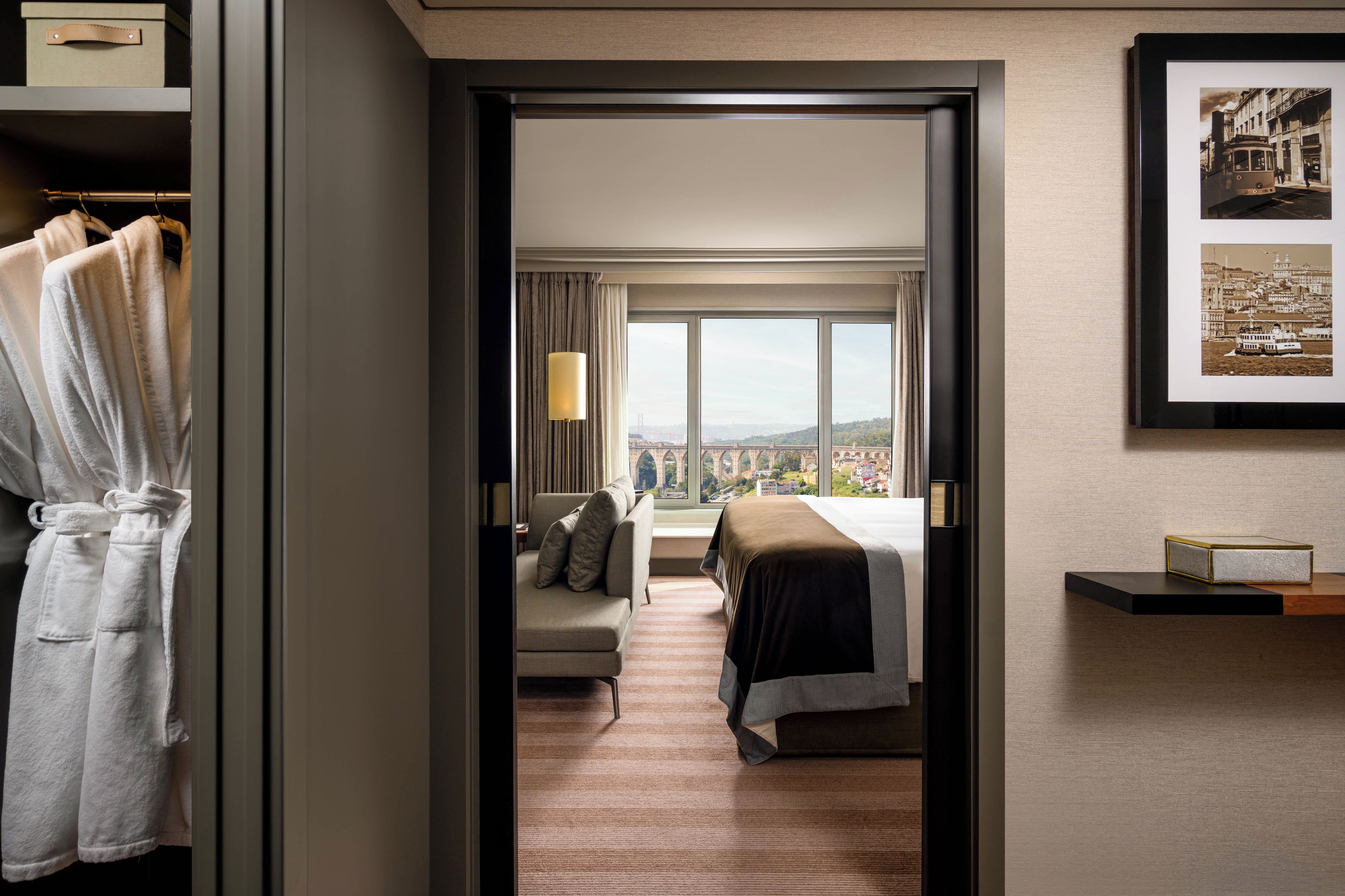 A hotel room with a bed, a sofa, a window with a view, and a framed picture on the wall.
