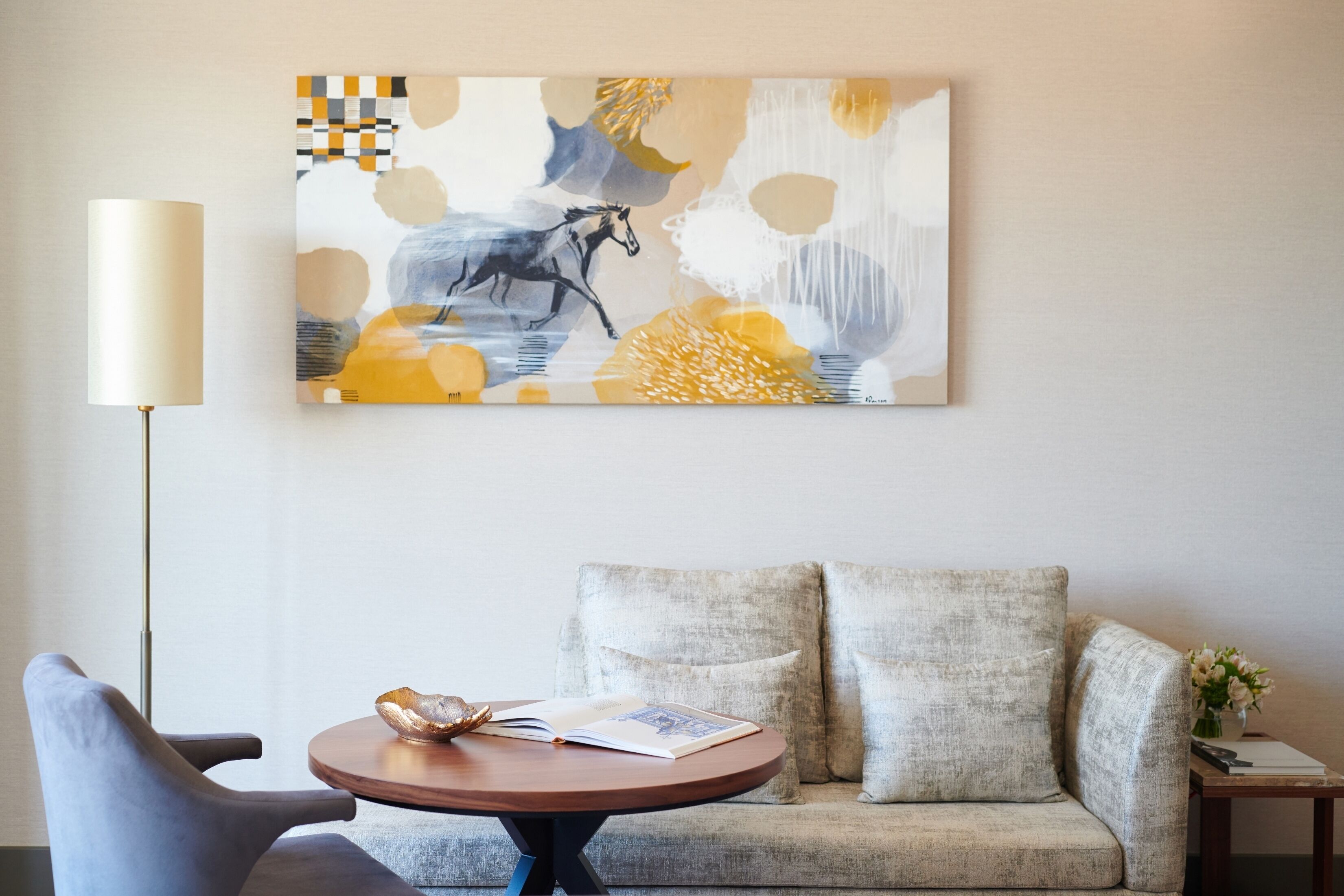 A modern living room with a sofa, a round coffee table, and a wall-mounted abstract painting.