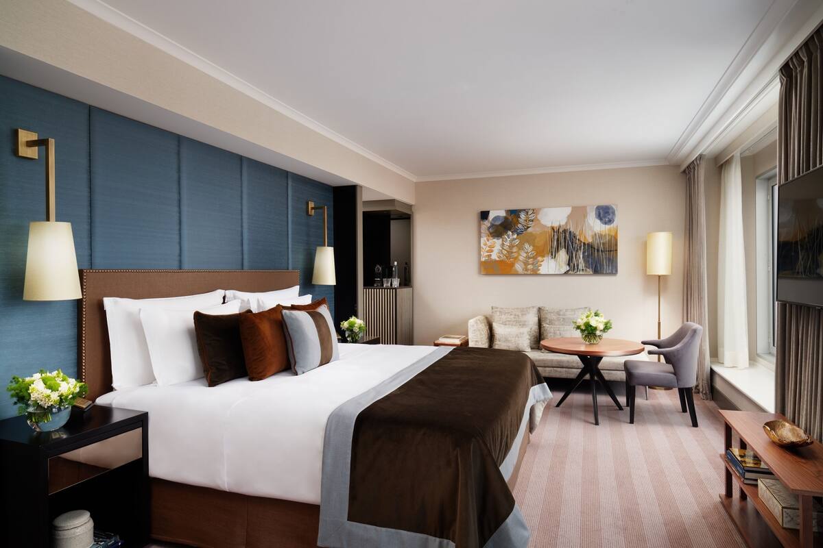 A hotel room with a large bed, a sofa, a small round table, and a TV.