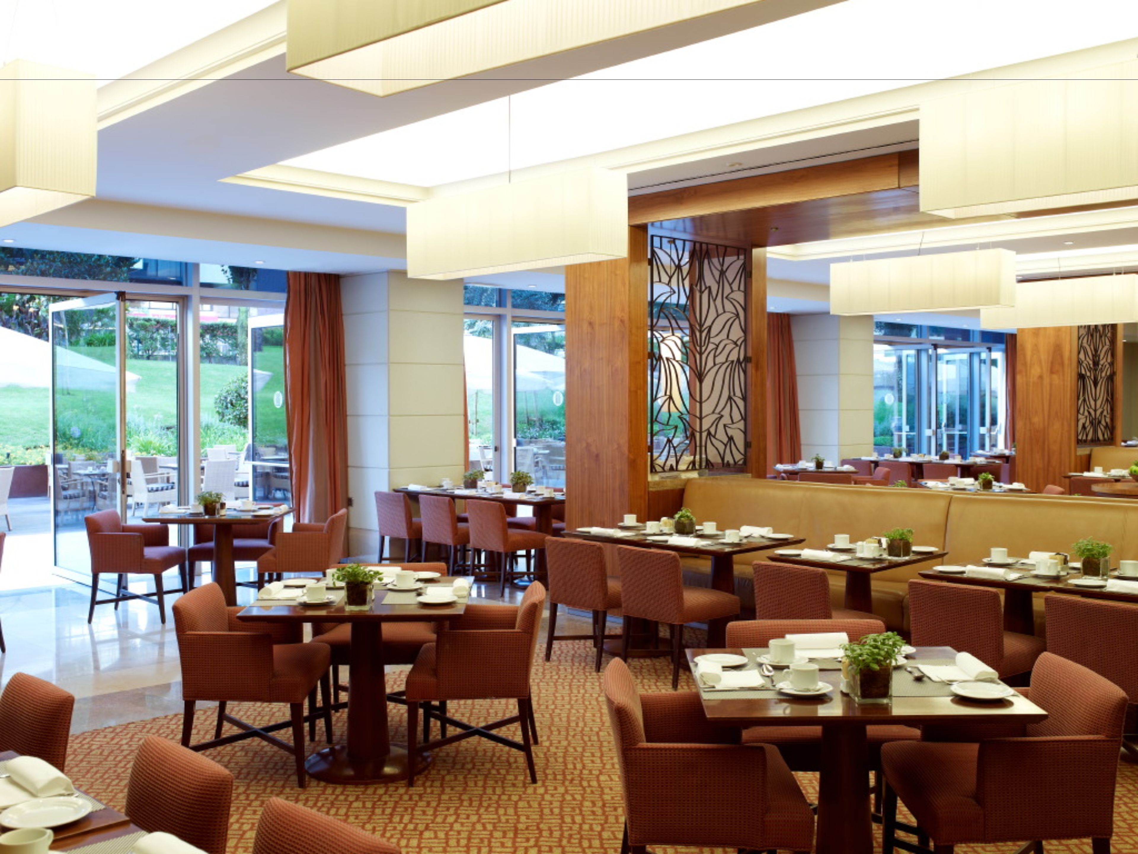 A modern restaurant with multiple dining areas, large windows, and a mix of indoor and outdoor seating.