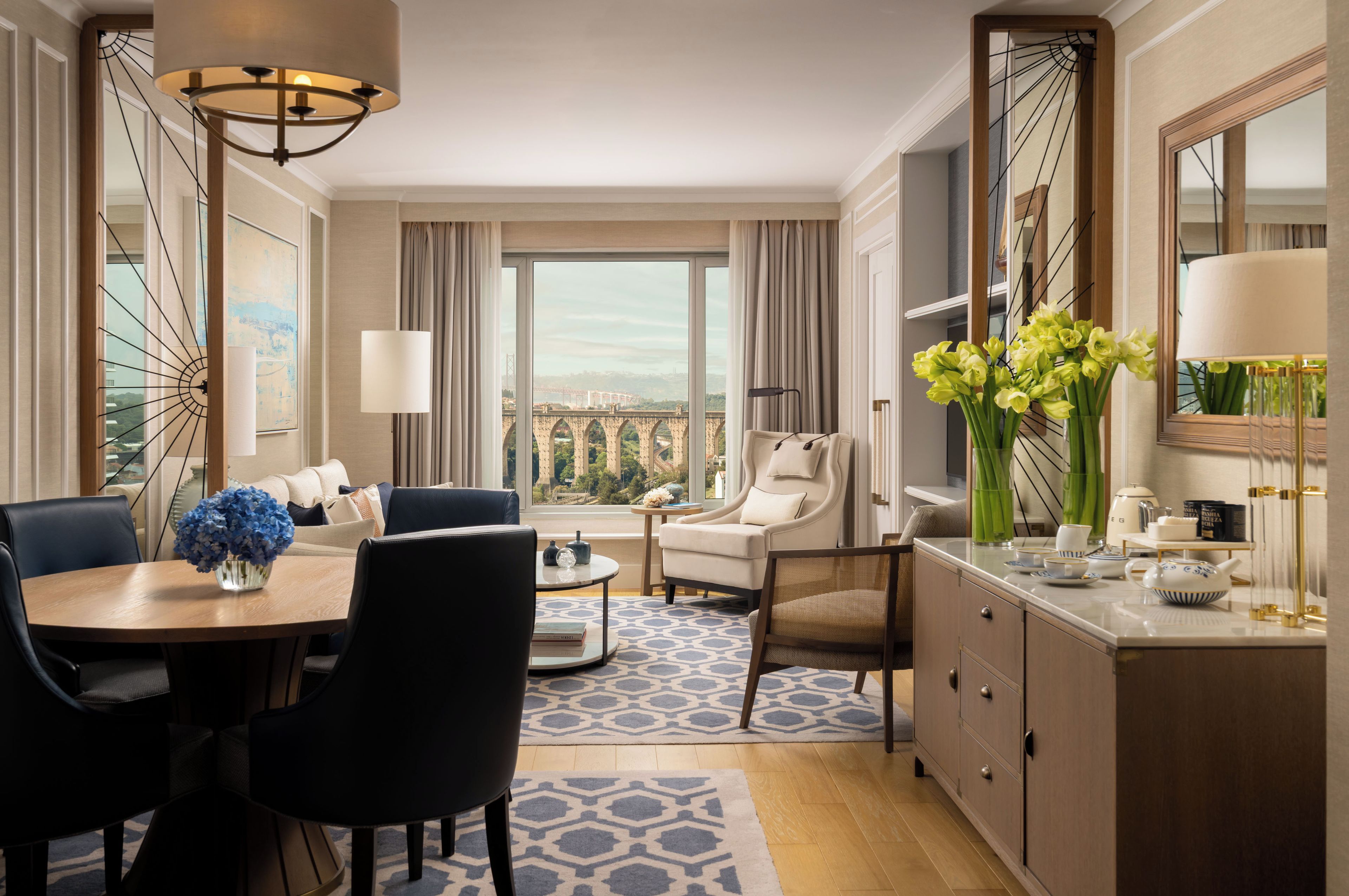 A hotel room with a dining area, a seating area with a view, and a large window.