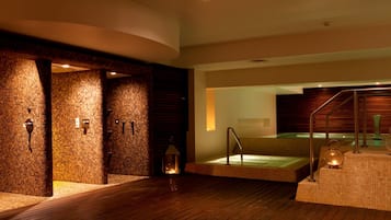 Un área de spa con piso de madera, un jacuzzi de vidrio y una pared de ladrillo.