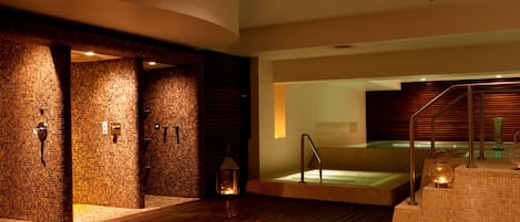 A spa area with a wooden floor, a glass-enclosed hot tub, and a brick wall.