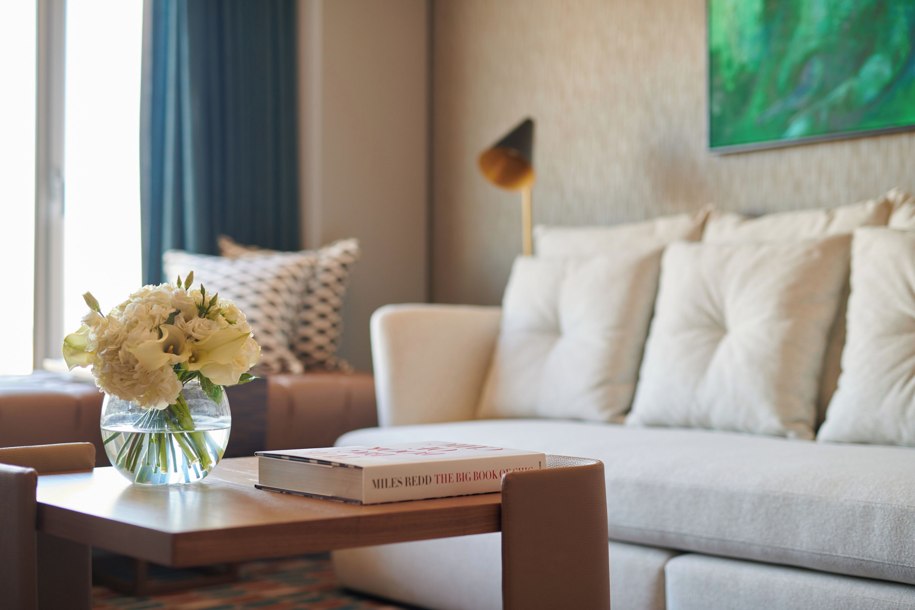 A living room with a sofa, a coffee table with a book and a vase of flowers.