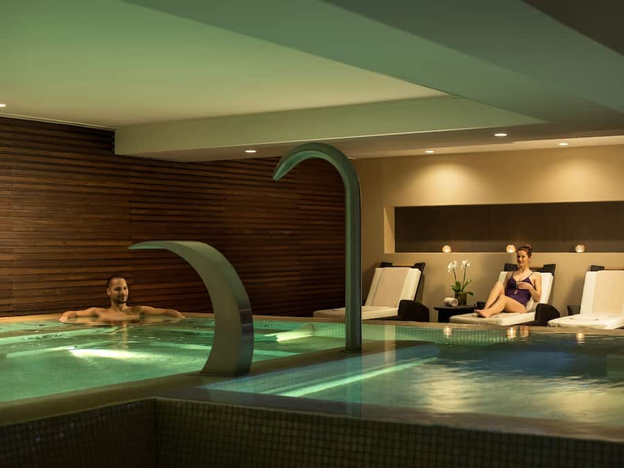 Una piscina interior moderna amb un aixeta corba i original, panells de fusta a les parets i dues gandules.