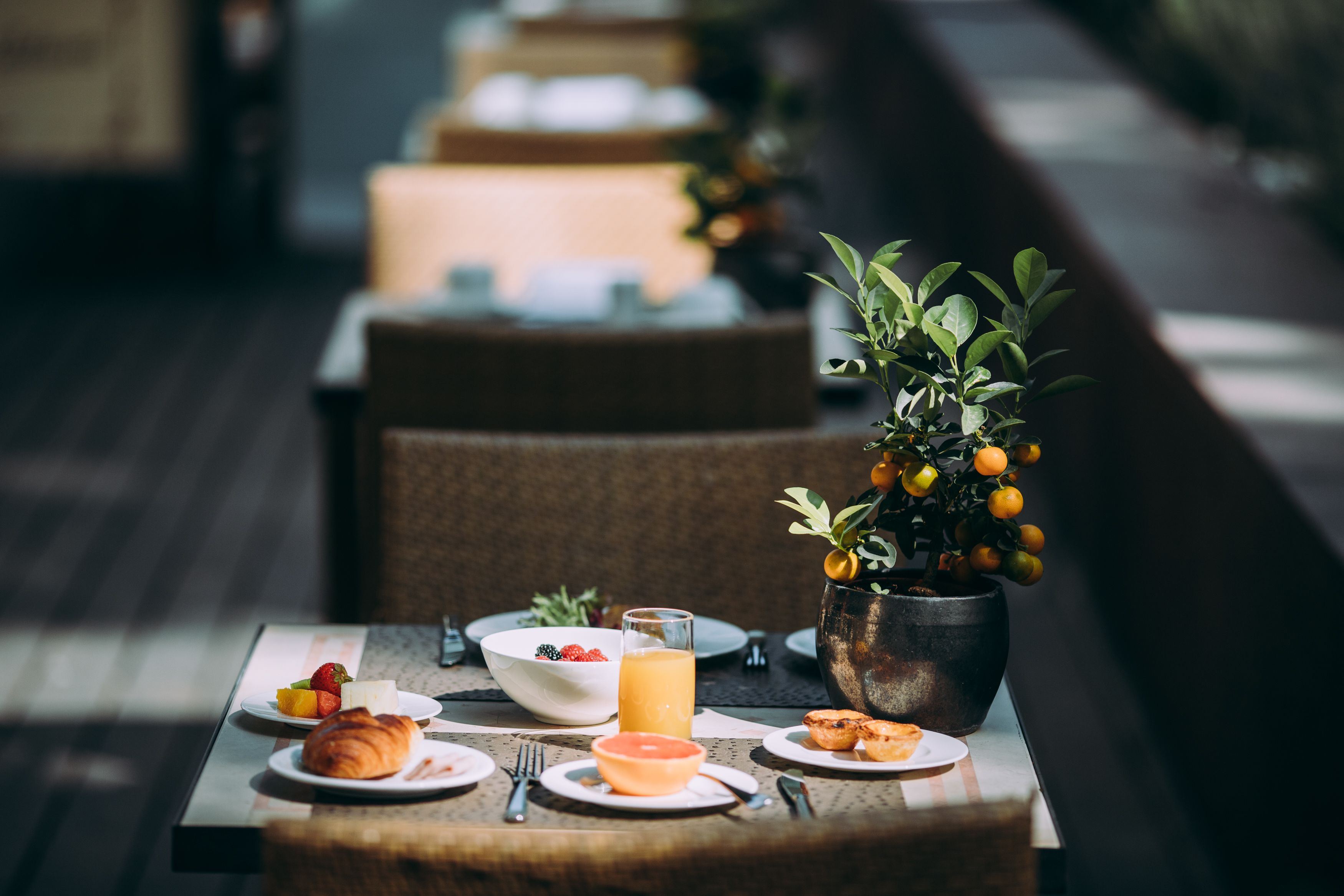 A breakfast setting with a table set for two, including croissants, fruit, and a glass of orange juice.