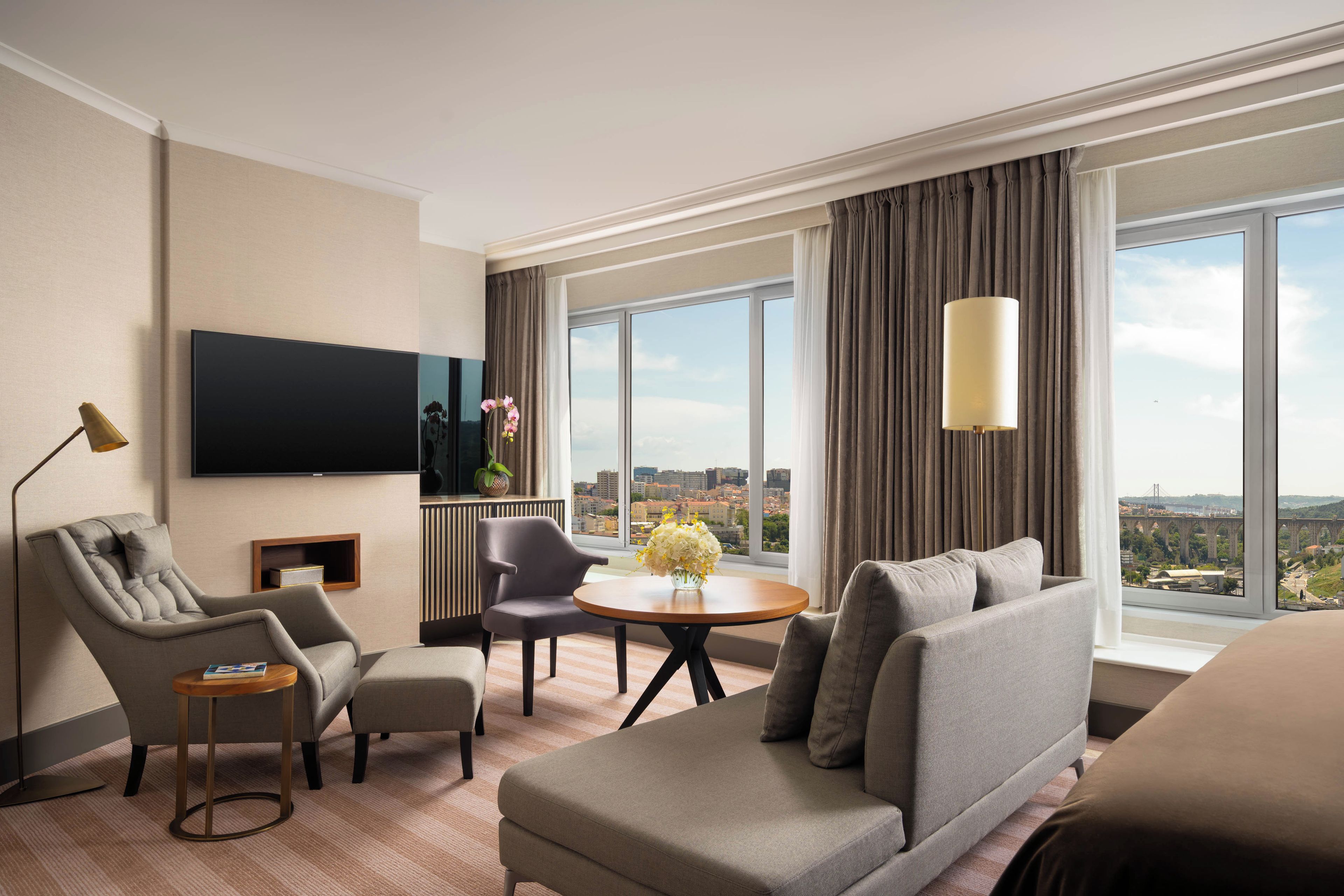 Een hotelkamer met een groot raam, een flatscreen televisie, een bank, een stoel, een tafeltje en een lamp.