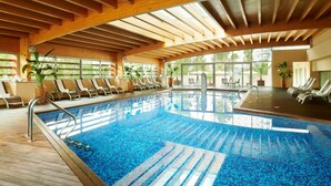 Una piscina interior con vigas de madera, sillas de descanso y plantas en macetas.