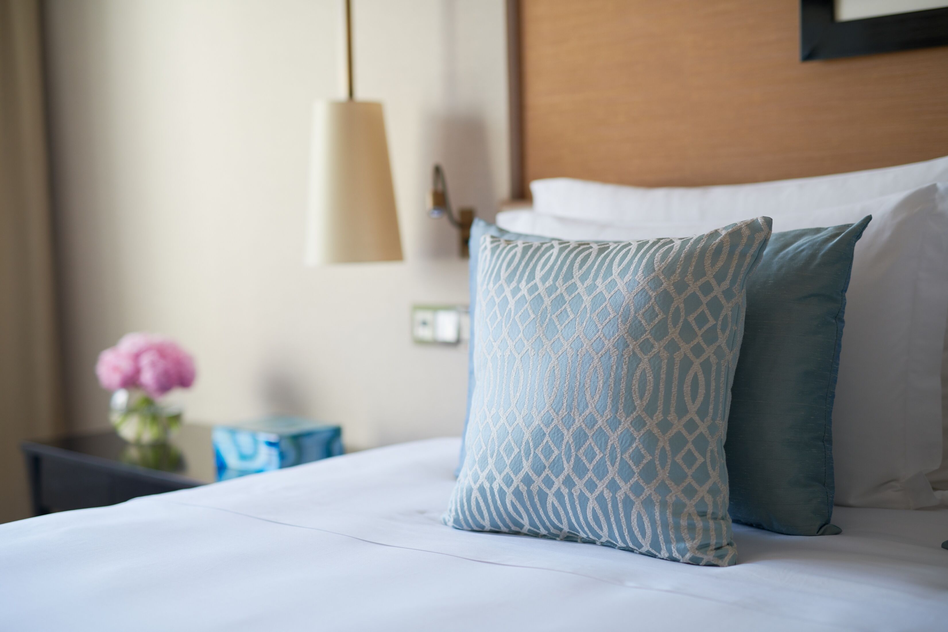 A neatly made bed with patterned pillows, a bedside table with a vase of flowers, and a hanging lamp.