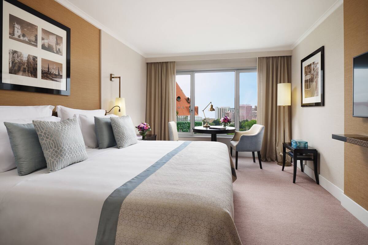 A hotel room with a large bed, a desk, a chair, and a TV.