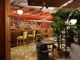 Una zona de bar con mostrador de madera, varios taburetes y una variedad de botellas y vasos.
