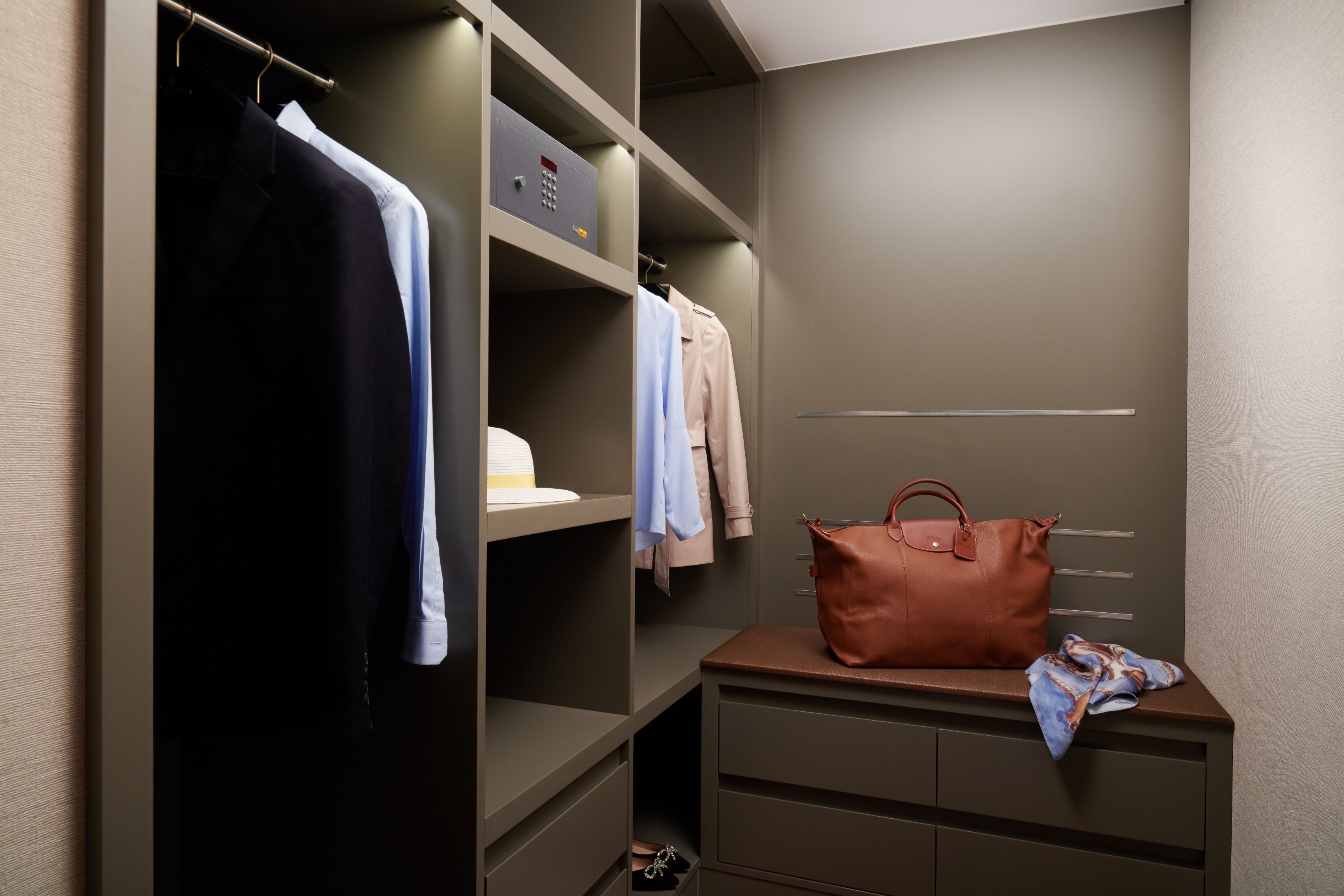 Een inloopkast met hangende kleding, planken en een tafeltje met een handtas en sjaal.