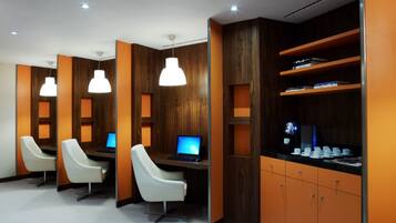 A modern office space with three white chairs, a desk with a computer, and a shelf with books and cups.