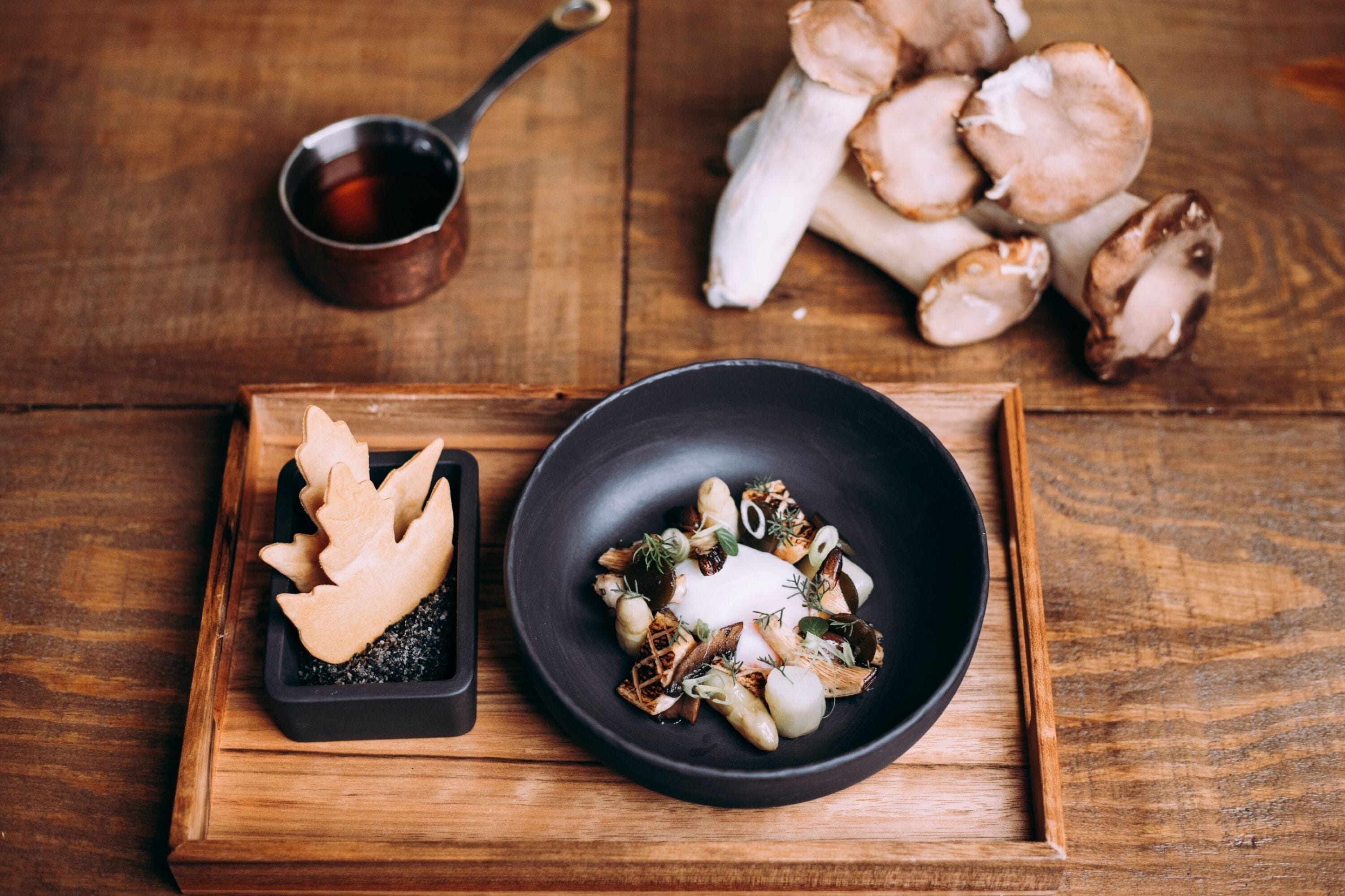 A wooden tray with a black bowl of mushrooms and a small dish of sliced mushrooms.
