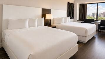 Een hotelkamer met twee bedden, een bureau, een stoel, een lamp en uitzicht op de stad.