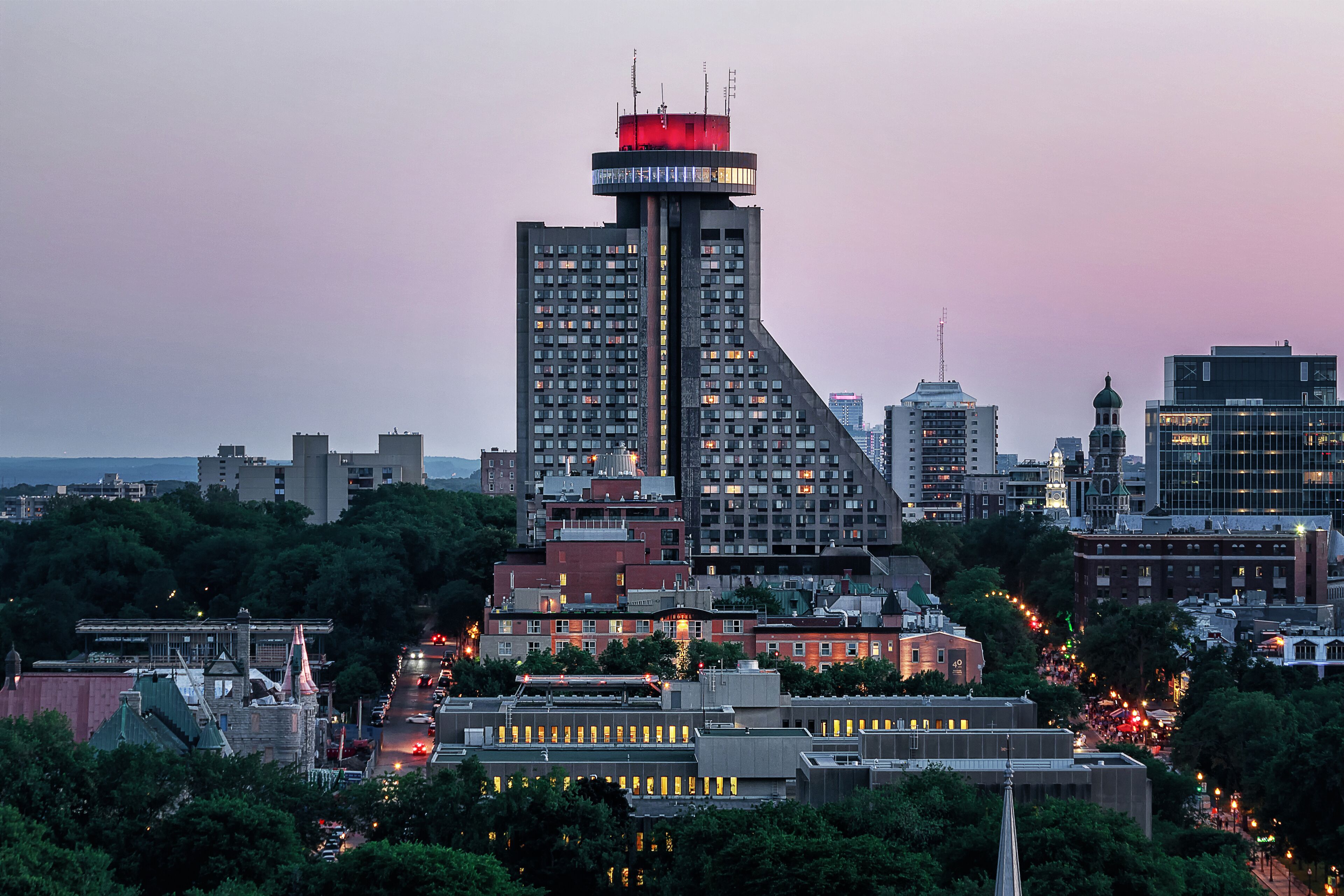 A cityscape with a prominent building featuring a unique architectural design, surrounded by other buildings and trees.