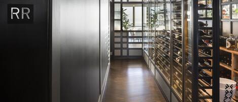 A hallway with a wooden floor, a glass wine rack on the right, and a sign with the letters "RR" on the left.