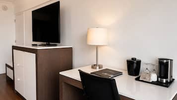 Habitación de hotel con escritorio, televisión, lámpara, cafetera y cesto de basura.