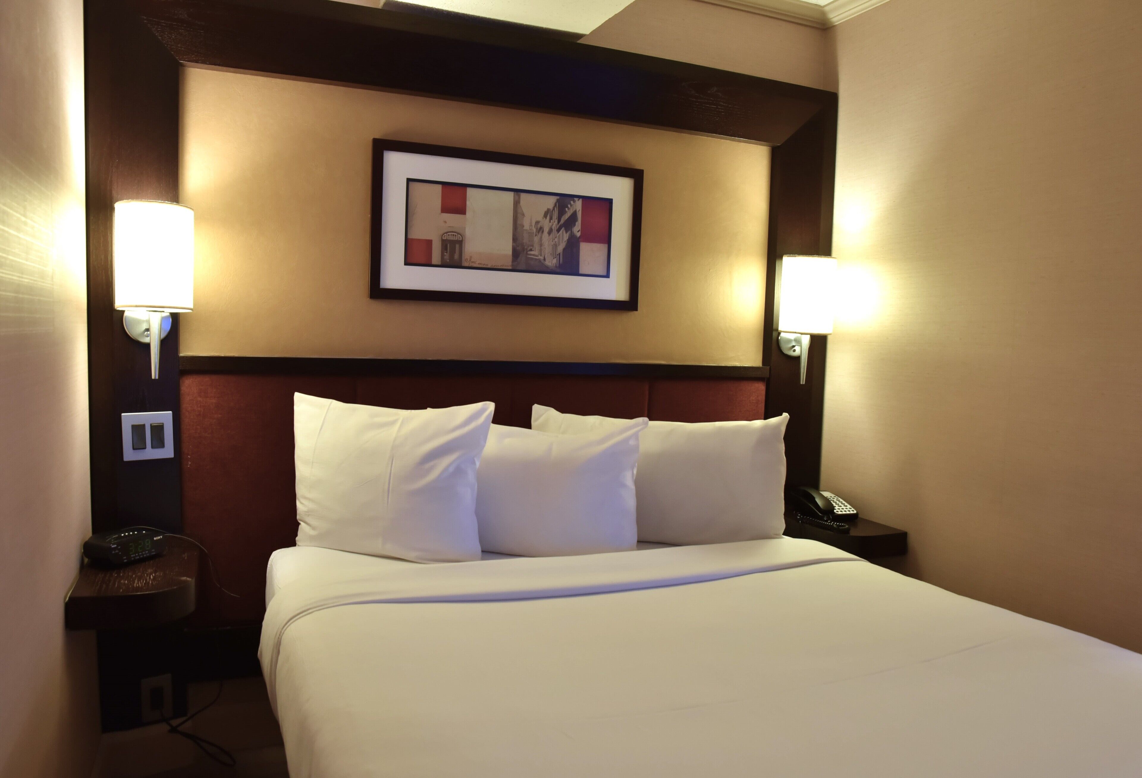 Habitación de hotel con una cama grande, dos lámparas de noche, un cuadro en la pared y un teléfono en la mesita de noche.