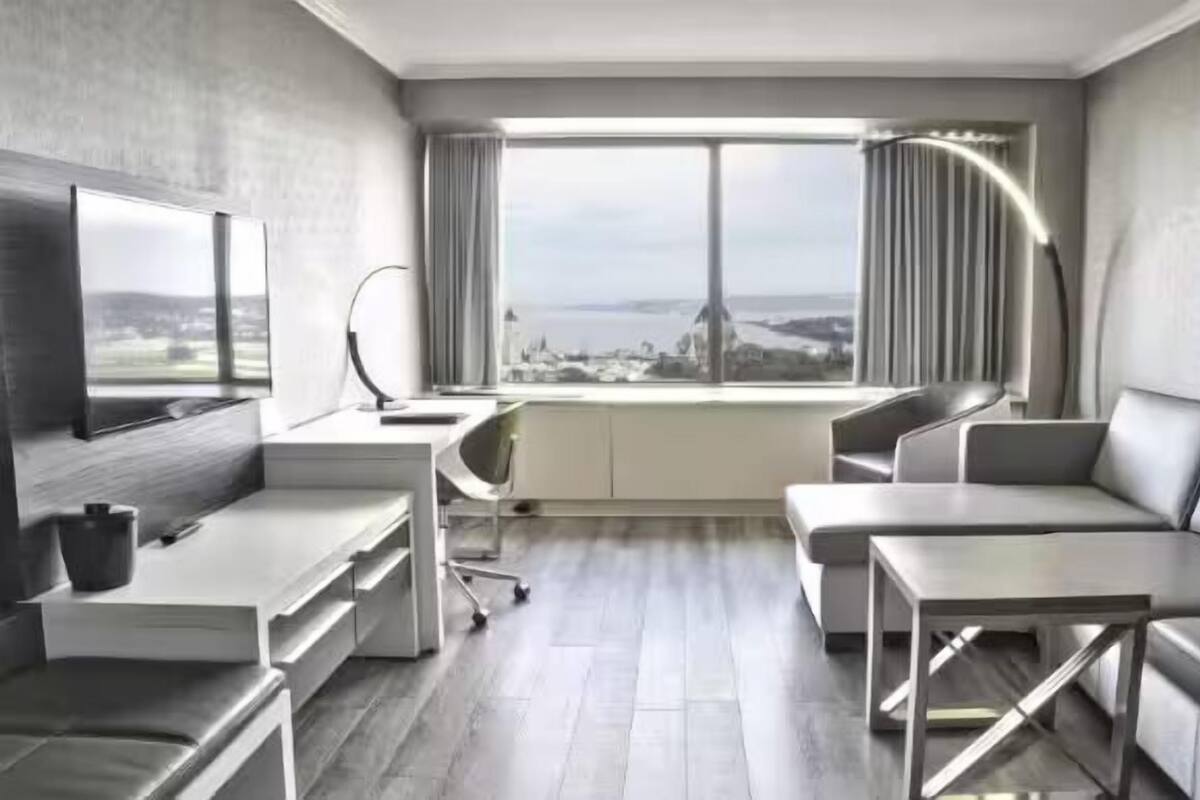 A modern hotel room with a large window, a desk, a sofa, and a TV.