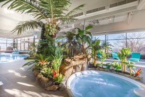 An indoor swimming pool with a waterfall feature, surrounded by tropical plants and stone structures. - Hôtel Le Concorde Québec (Québec City)
