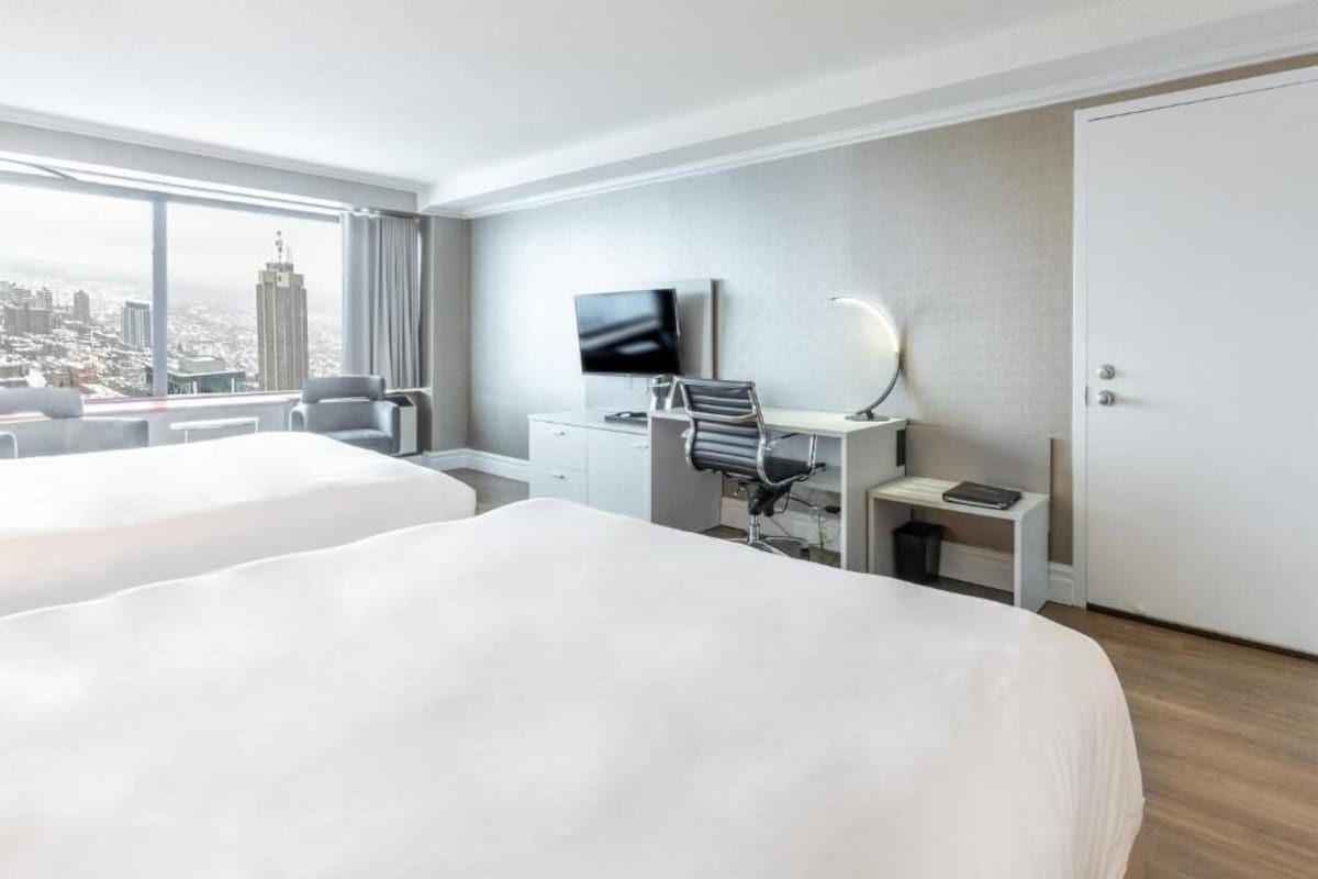 A hotel room with two beds, a desk with a computer, a TV, and a city view.