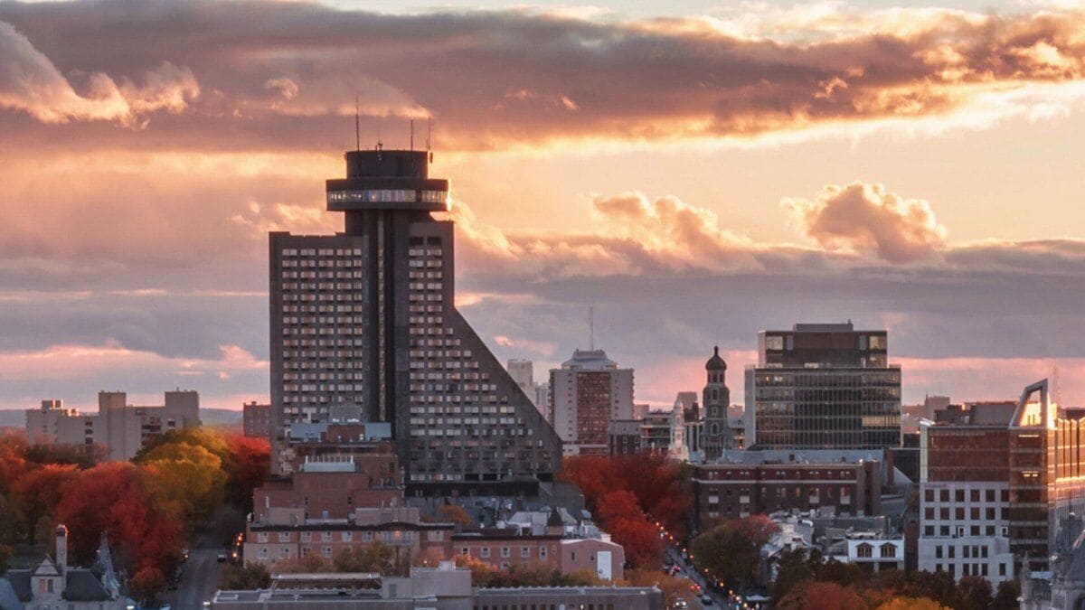 A cityscape with a prominent building featuring a unique architectural design, surrounded by other buildings and autumn foliage.