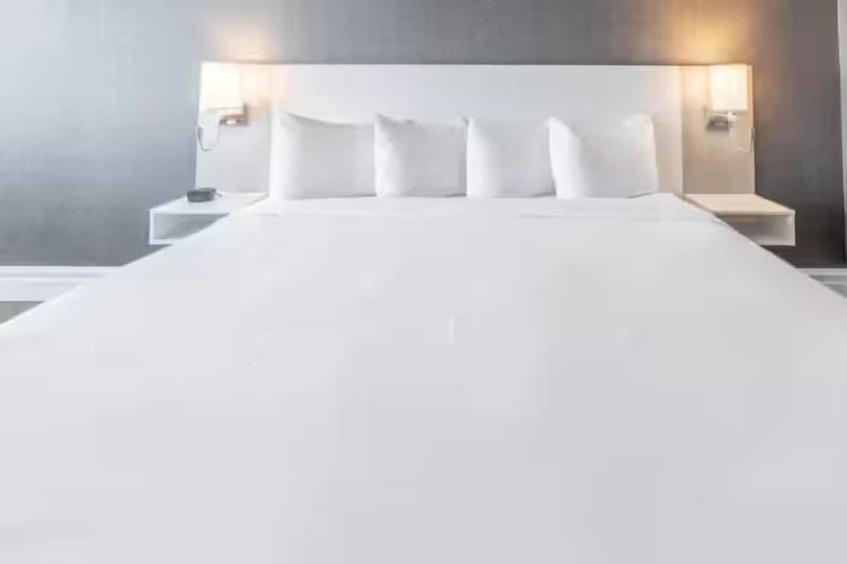 A large bed with white linens and a headboard with two wall-mounted lamps.