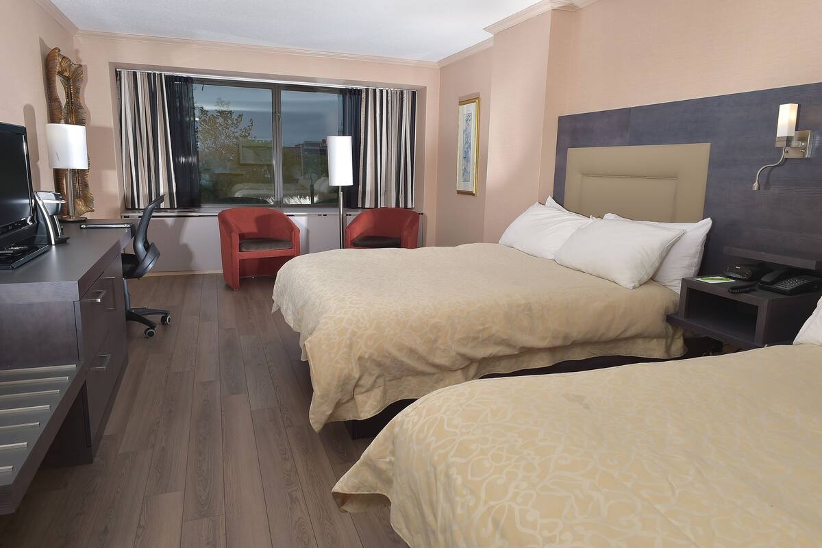A hotel room with two beds, a desk with a computer, a chair, and a window with curtains.
