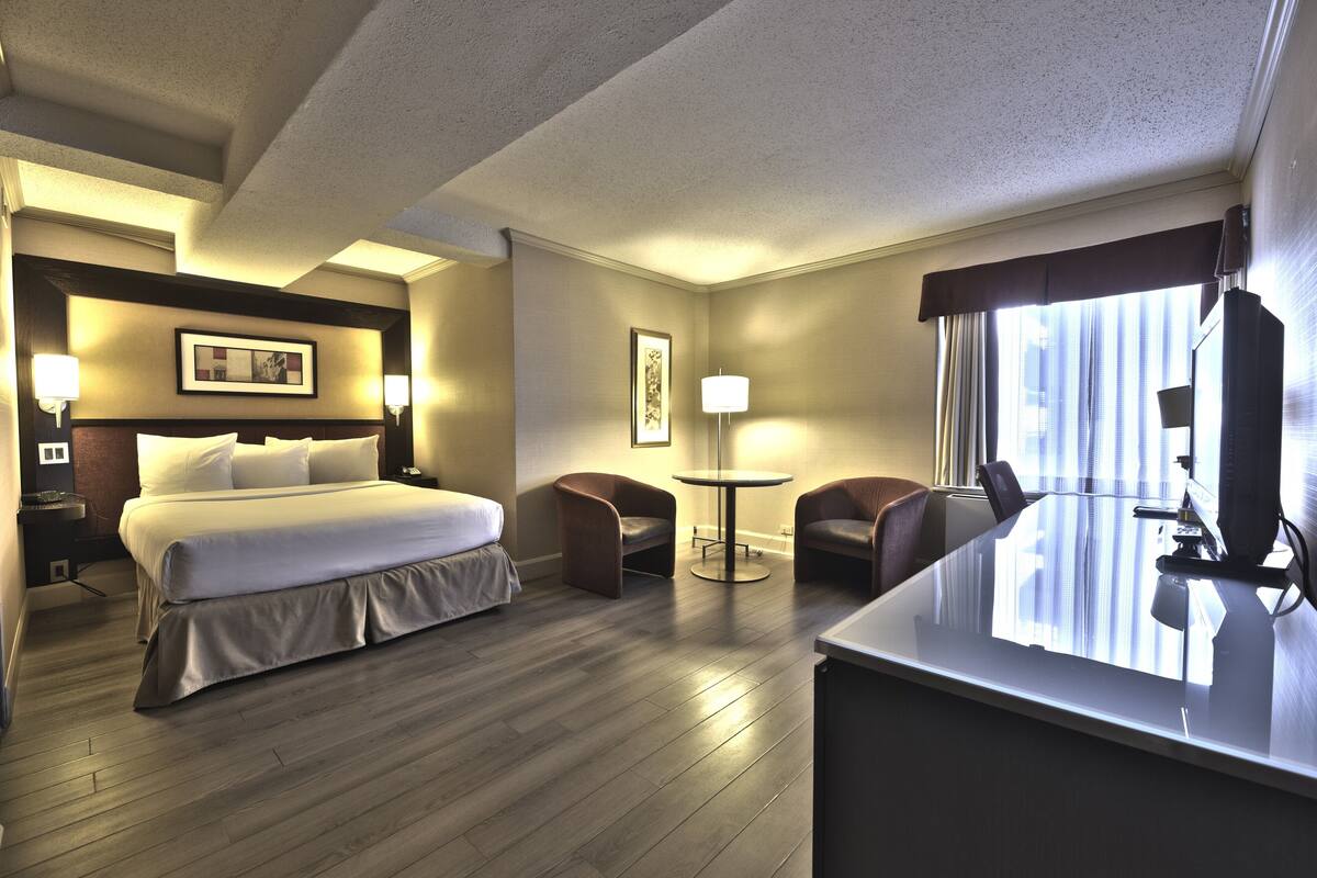 A hotel room with a large bed, two armchairs, a small table, and a desk with a computer.