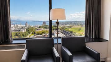 Ein Zimmer mit zwei schwarzen Ledersesseln, einer Stehlampe und einem großen Fenster mit Blick auf die Stadt.