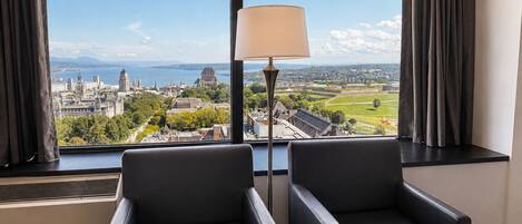 Una habitación con dos sillones de cuero negro, una lámpara de pie y un amplio ventanal con vistas a la ciudad.