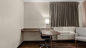 Een hotelkamer met een houten tafel, een stoel, een lamp, een bank en een raam met gordijnen.