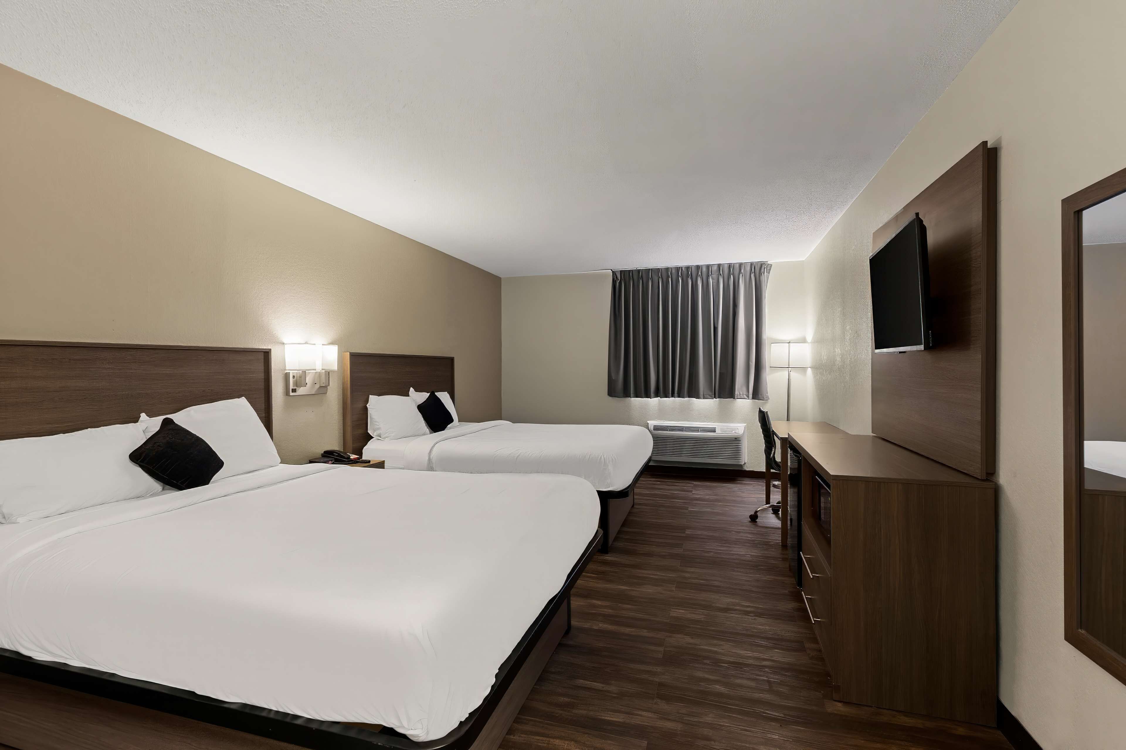A hotel room with two beds, a TV, a desk, and a window with curtains.
