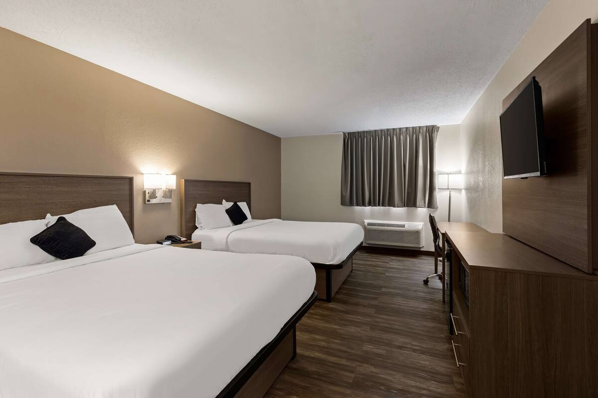 A hotel room with two beds, a desk, a chair, a TV, and a window with curtains.
