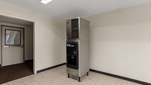 Een compact, modern apparaat voor ijsdispensatie in een gang met betegelde vloer en een deur naar een andere kamer.