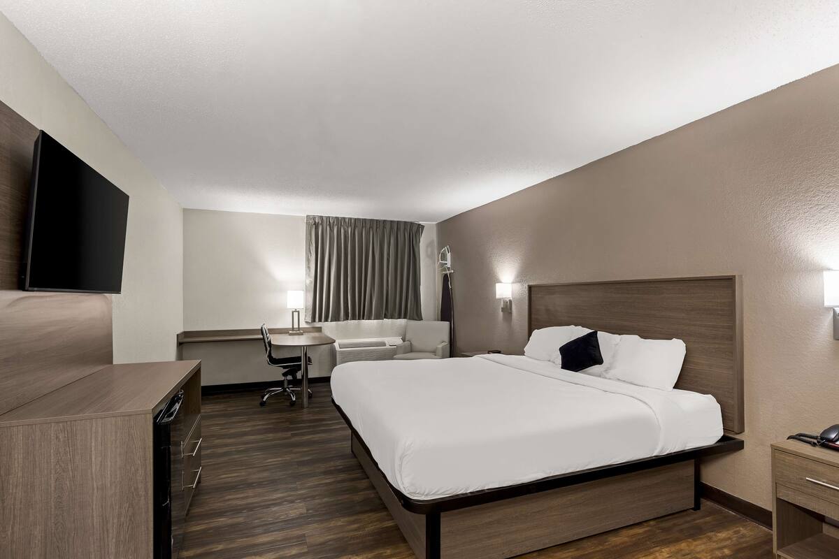 A hotel room with a bed, bedside table, desk, chair, and a flat-screen TV.