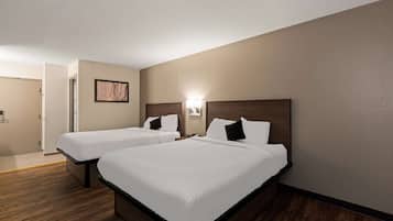 A hotel room with two beds, wooden flooring, a painting on the wall, and a nightstand with a lamp.
