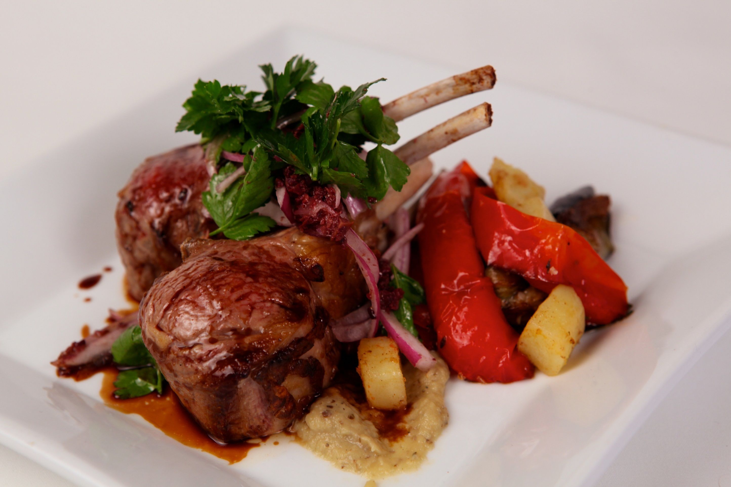 Une assiette de nourriture comprenant des côtelettes d’agneau, des poivrons rouges et des pommes de terre.