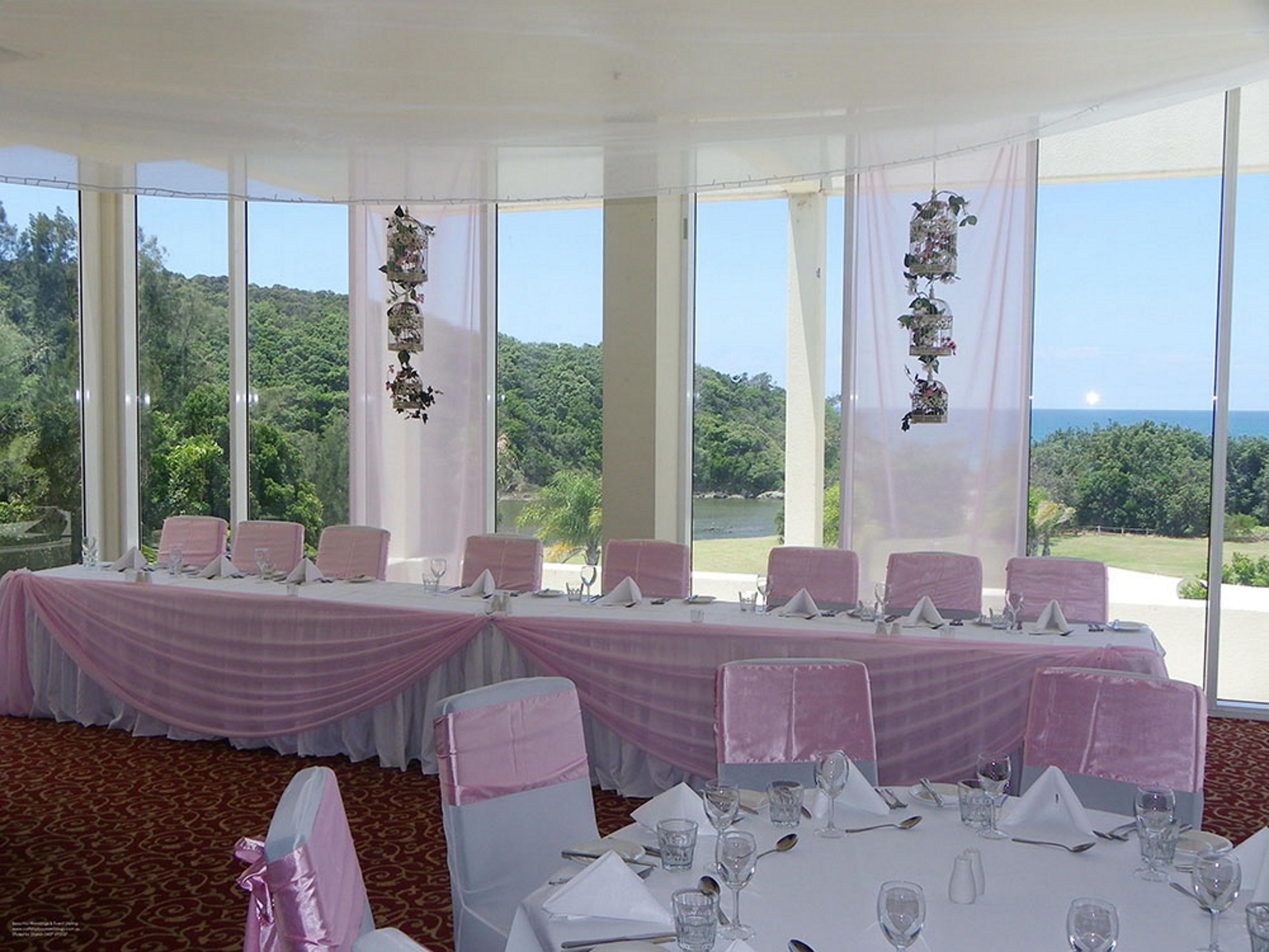 Un salón de banquetes con mesas dispuestas para un evento formal, amplias ventanas que ofrecen vista a un paisaje exuberante.
