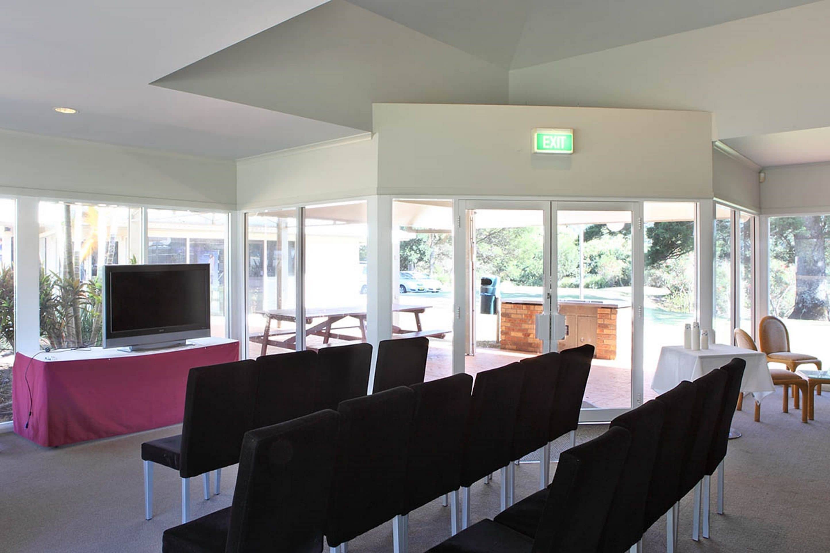 Un salón de conferencias con una televisión, sillas, una mesa y vistas al exterior.