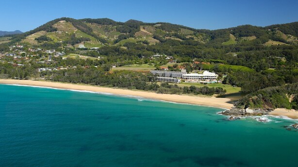 A coastal resort with a beachfront view, a large building with multiple floors, and surrounding hills. - Opal Cove Resort (Korora)