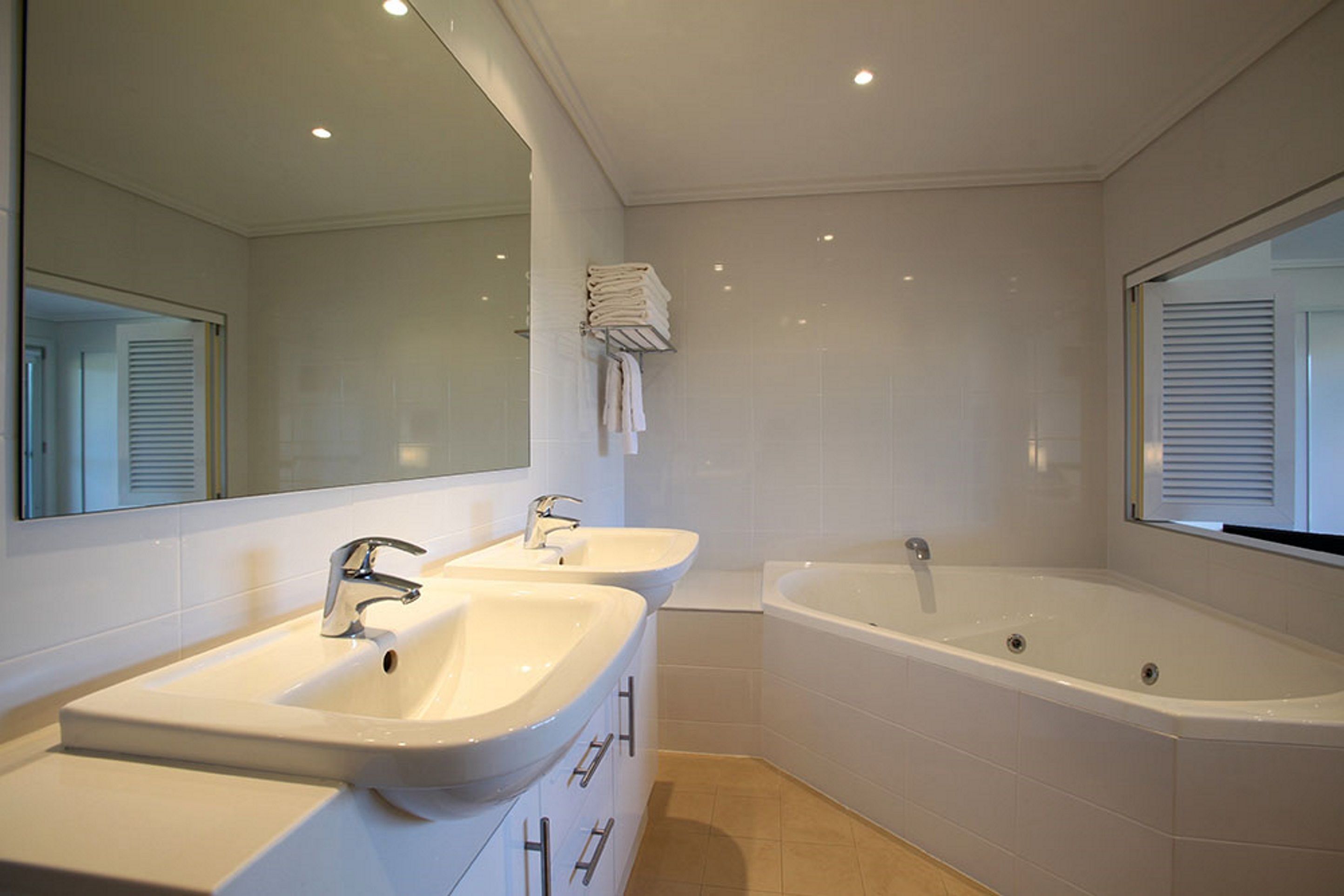Un baño moderno con dos lavamanos, una bañera grande y un espejo.