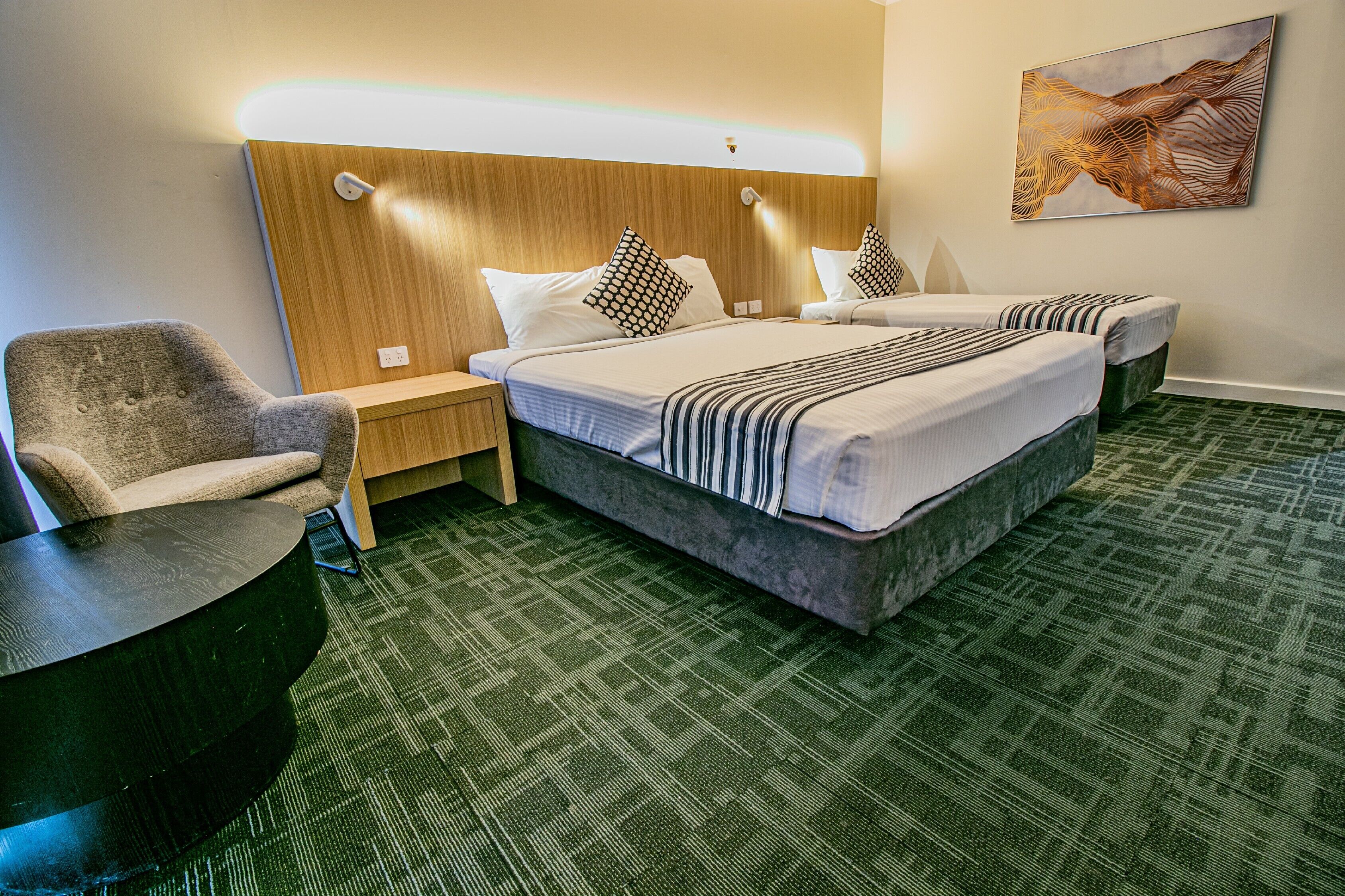 Una habitación de hotel con una cama grande, dos mesitas de noche, una silla y una alfombra verde.